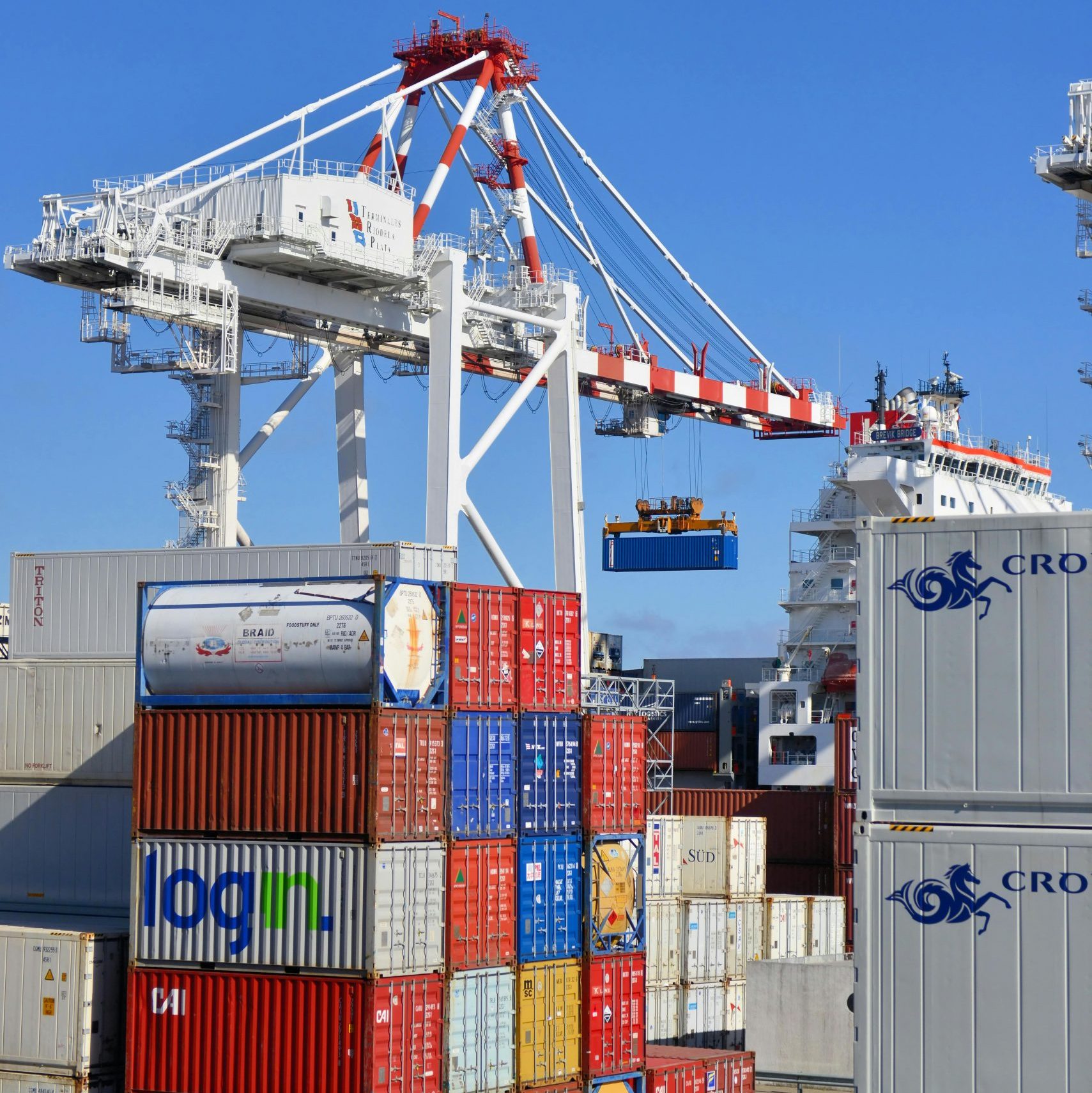 Colorful shipping containers stacked in a busy port with cranes overhead.