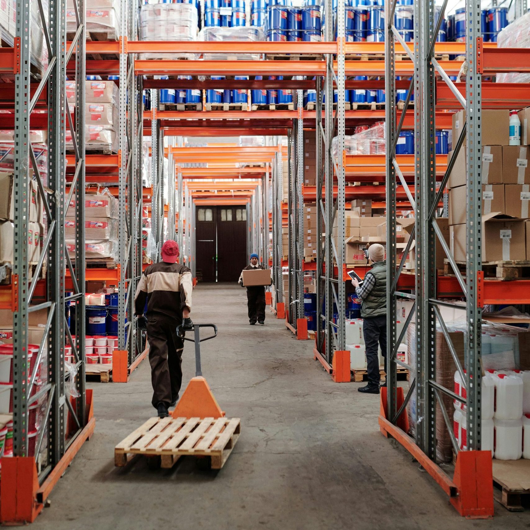 Workers arrange inventory on shelves in a large industrial warehouse.
