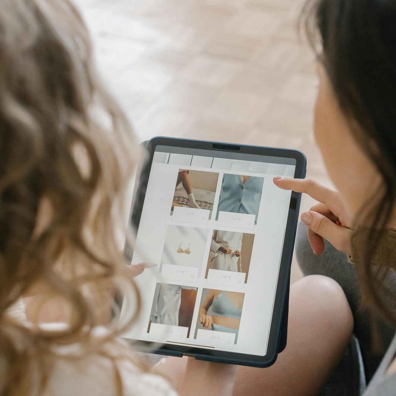 Two women sitting together, shopping online using a tablet, sharing ideas and browsing products.