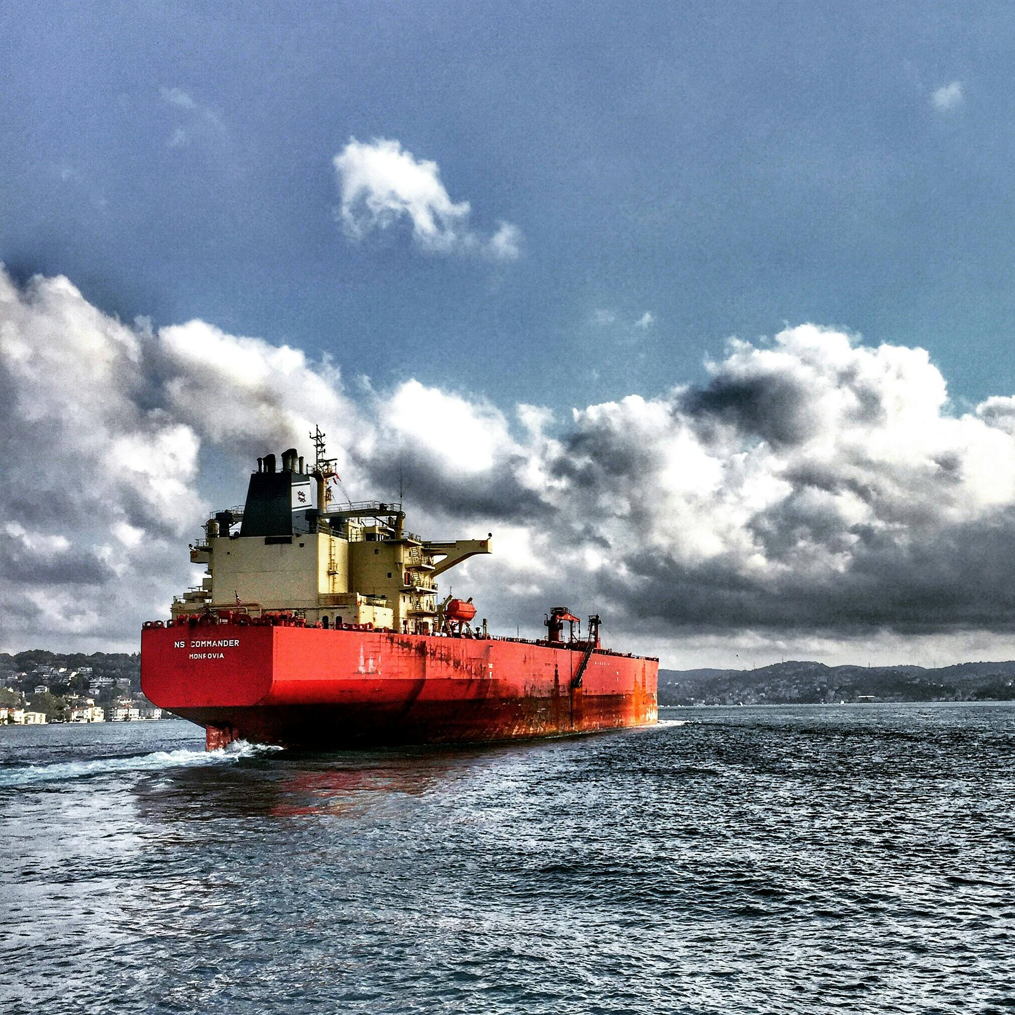 Red cargo ship navigating the Bosphorus under dramatic clouded sky, Turkey.